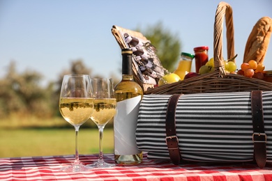 Photo of Picnic basket with wine, snacks and mat on table in park