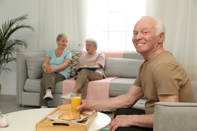 Elderly man having breakfast at nursing home, space for text. Assisting senior people