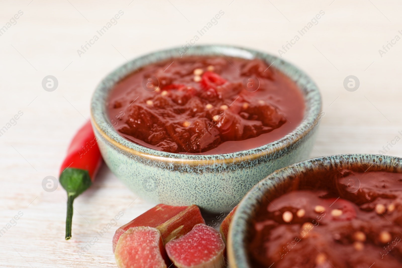 Photo of Tasty rhubarb sauce and ingredients on white wooden table, closeup