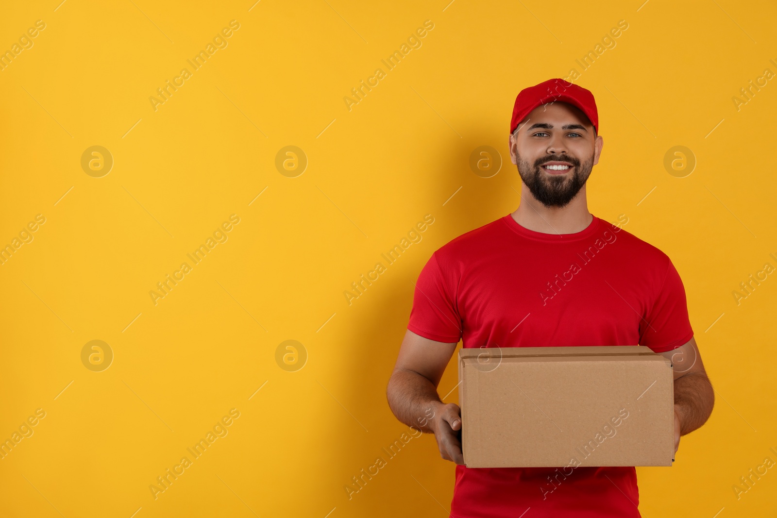 Photo of Courier holding cardboard box on yellow background, space for text