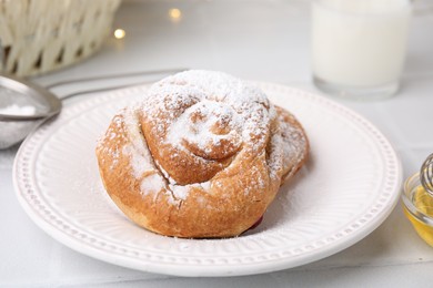 Photo of Delicious roll with sugar powder on white tiled table, closeup. Sweet bun