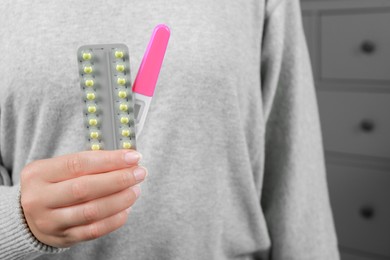 Woman holding birth control pills and pregnancy test indoors, closeup