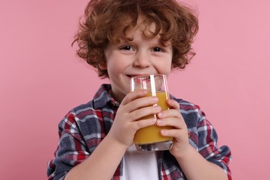 Cute little boy with glass of fresh juice on pink background