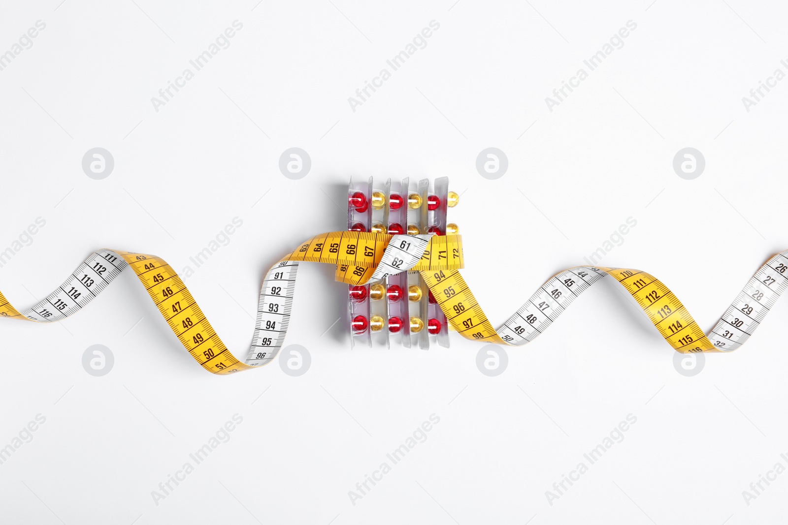 Photo of Weight loss pills in blister packs tied with measuring tape on white background, top view