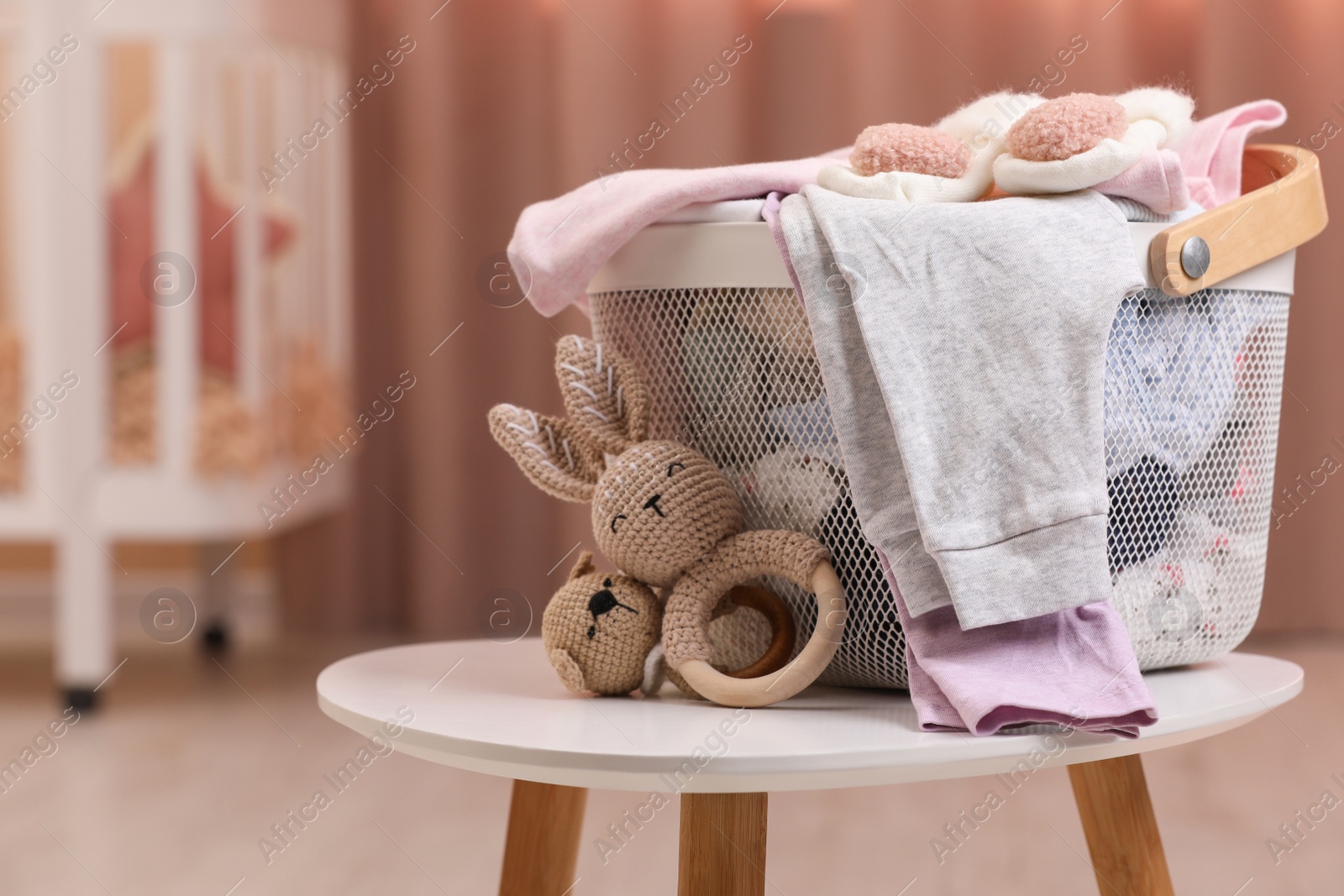 Photo of Laundry basket with baby clothes and crochet toys on white wooden table in child room, space for text