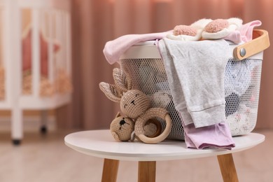 Laundry basket with baby clothes and crochet toys on white wooden table in child room, space for text