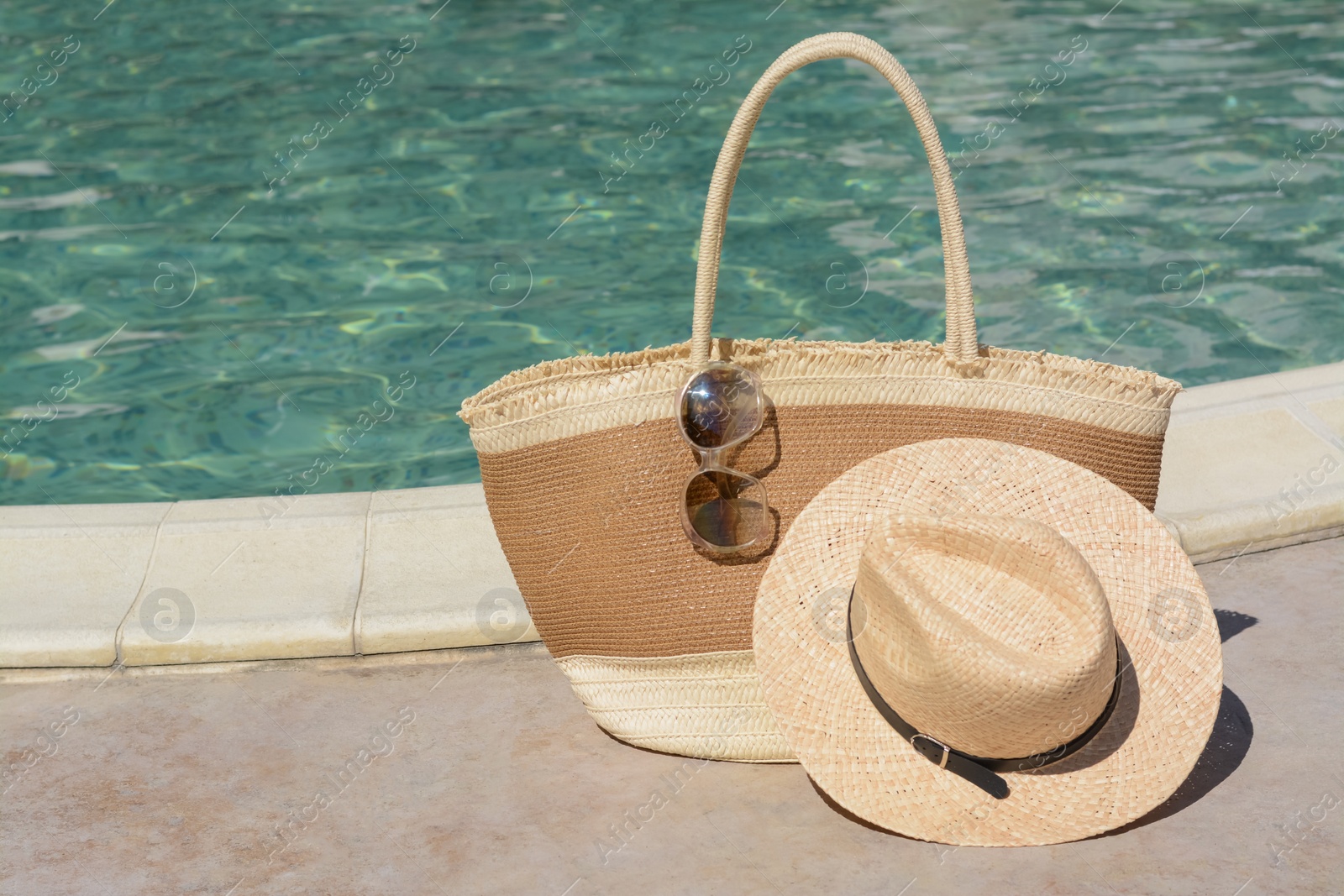 Photo of Stylish bag, sunglasses and hat near outdoor swimming pool on sunny day. Beach accessories