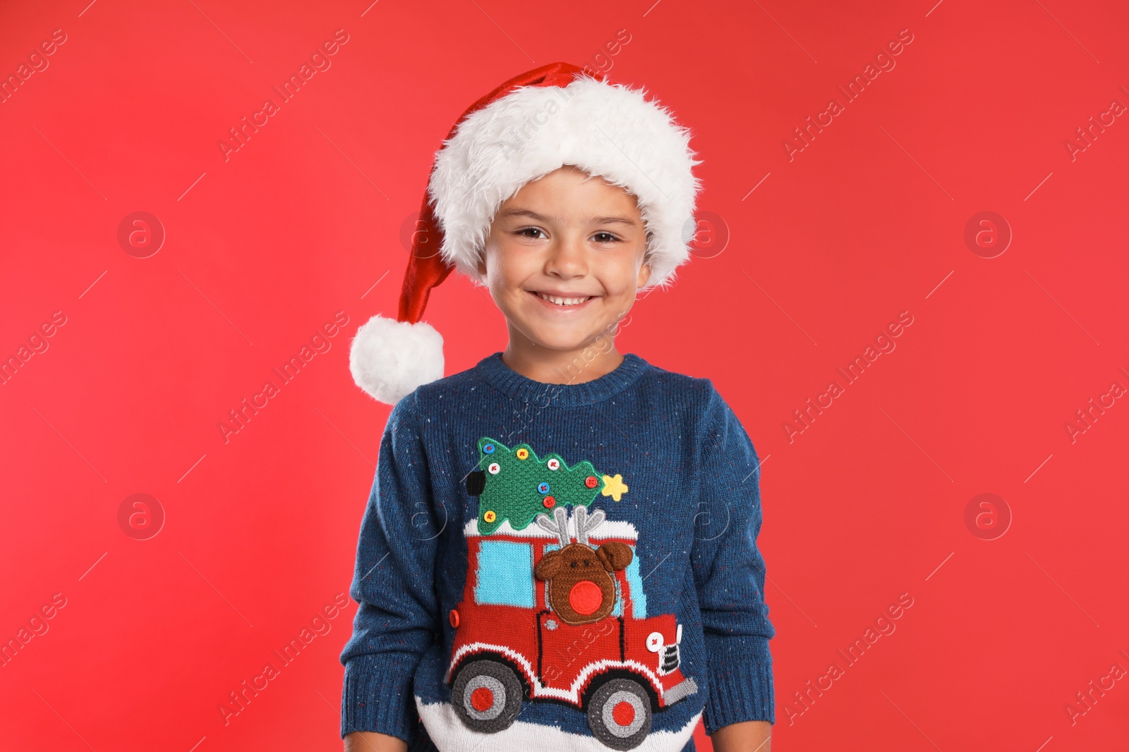 Photo of Happy little child in Santa hat on red background. Christmas celebration