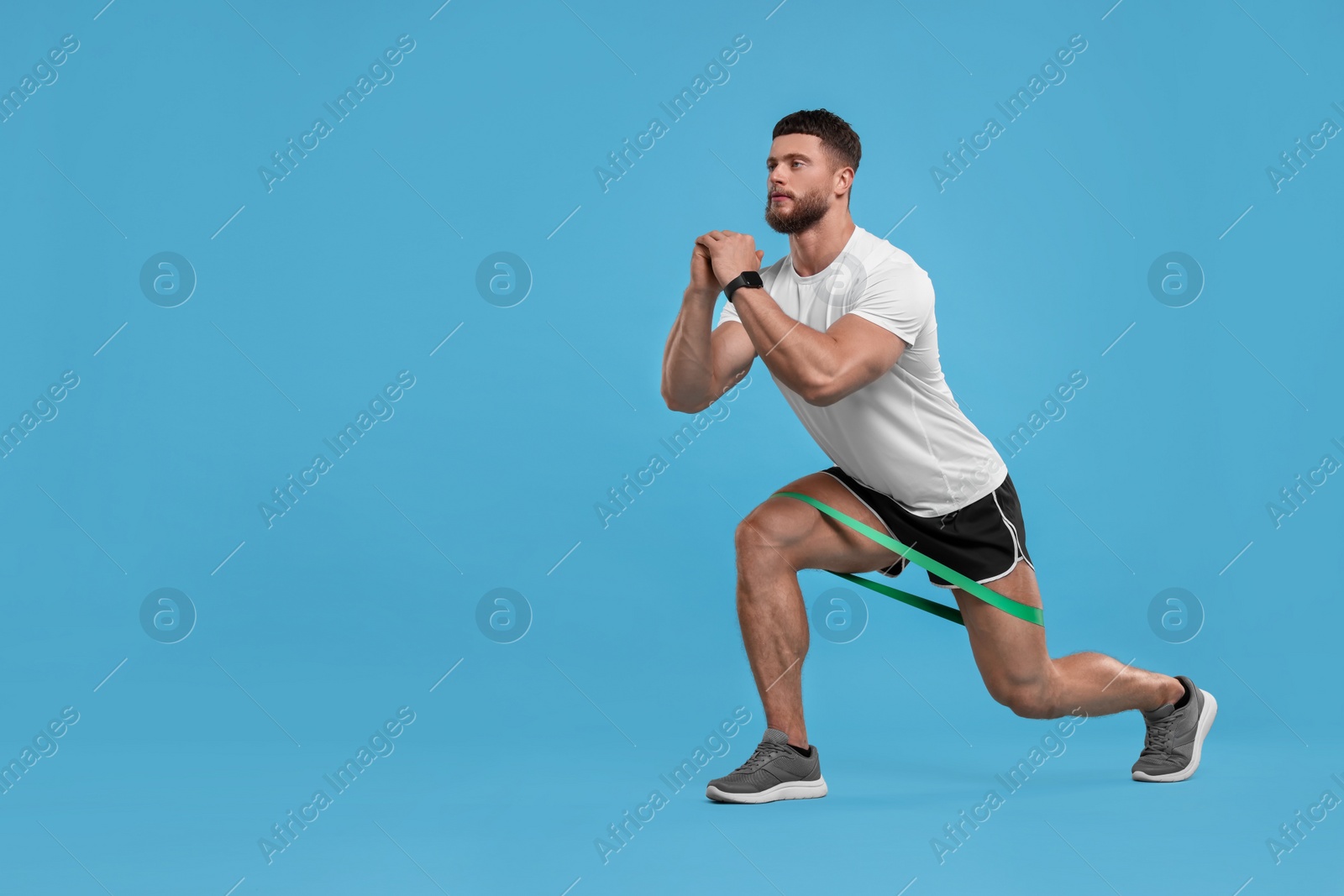 Photo of Young man exercising with elastic resistance band on light blue background. Space for text