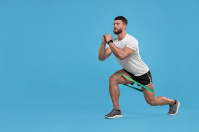 Young man exercising with elastic resistance band on light blue background. Space for text