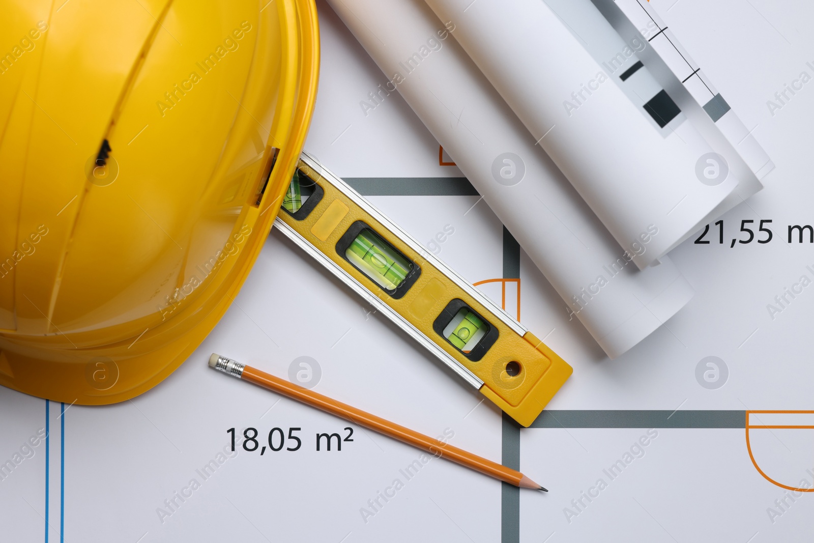 Photo of Rolled construction drawings, safety hat, pencil and bubble level on house plan, top view. Architect workspace