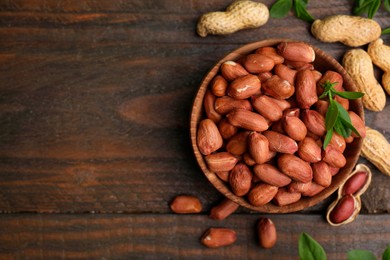 Photo of Fresh peanuts and leaves in bowl on wooden table, flat lay. Space for text