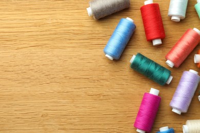 Photo of Many colorful sewing threads on wooden table, flat lay. Space for text