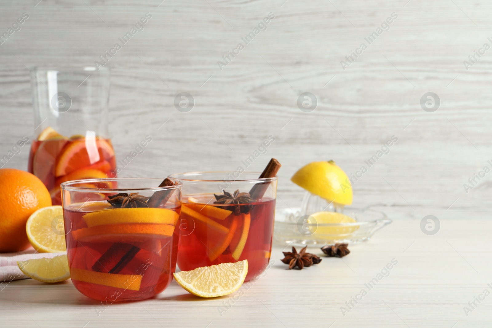 Photo of Aromatic punch drink and ingredients on white wooden table. Space for text