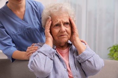 Photo of Nurse taking care of senior woman with headache indoors