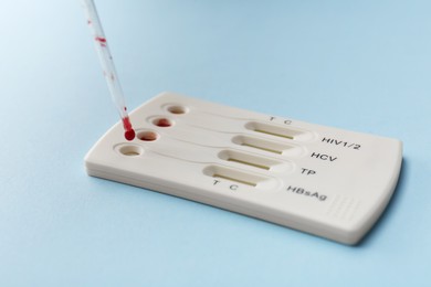 Dropping blood sample onto disposable multi-infection express test cassette with pipette on light blue background