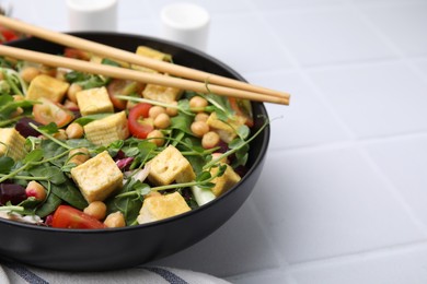 Photo of Bowl of tasty salad with tofu, chickpeas and vegetables on white tiled table, closeup. Space for text