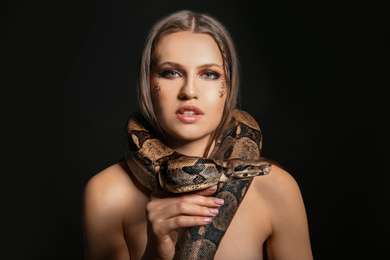 Beautiful woman with boa constrictor on black background