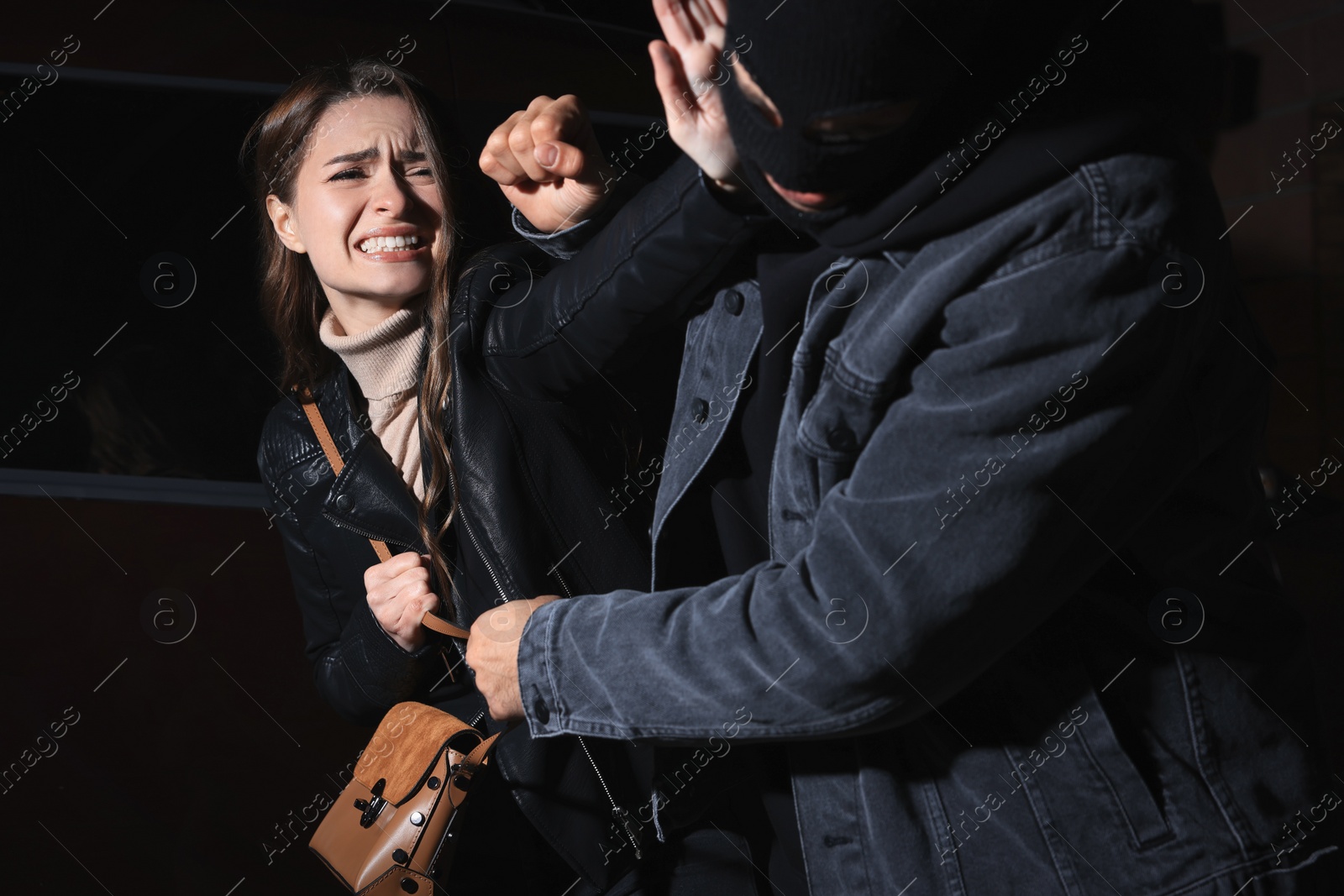 Photo of Woman fighting with thief while he trying to steal her bag outdoors at night. Self defense concept