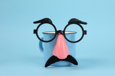 Photo of Man's face made of cup, fake mustache, nose and glasses on light blue background