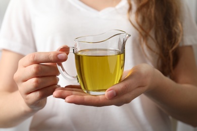 Photo of Young woman holding jug of fresh olive oil, closeup