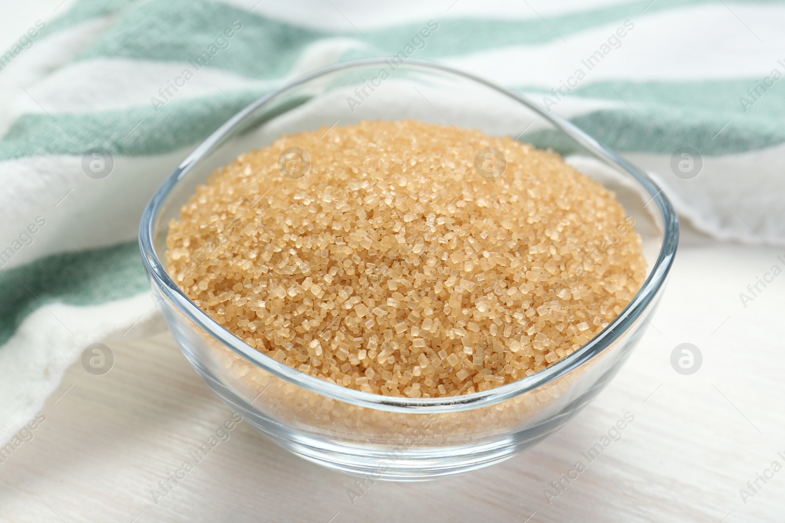 Photo of Brown sugar in glass bowl on white wooden table, closeup