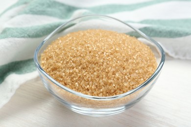 Brown sugar in glass bowl on white wooden table, closeup