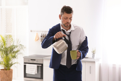 Photo of Sleepy man pouring coffee into cup at home in morning