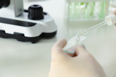 Photo of Lab assistant dropping liquid on microscope slide at table, closeup. Plant chemistry