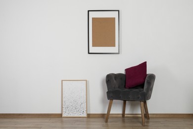 Photo of Comfortable armchair, cushion and picture frames indoors. Interior design