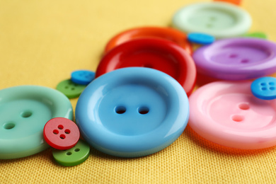 Many bright sewing buttons on yellow fabric, closeup