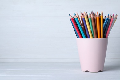 Photo of Colorful pencils in cup on white wooden table. Space for text