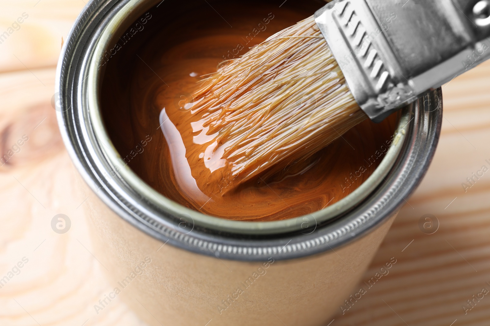 Photo of Dipping brush into can with wood stain on wooden surface, closeup