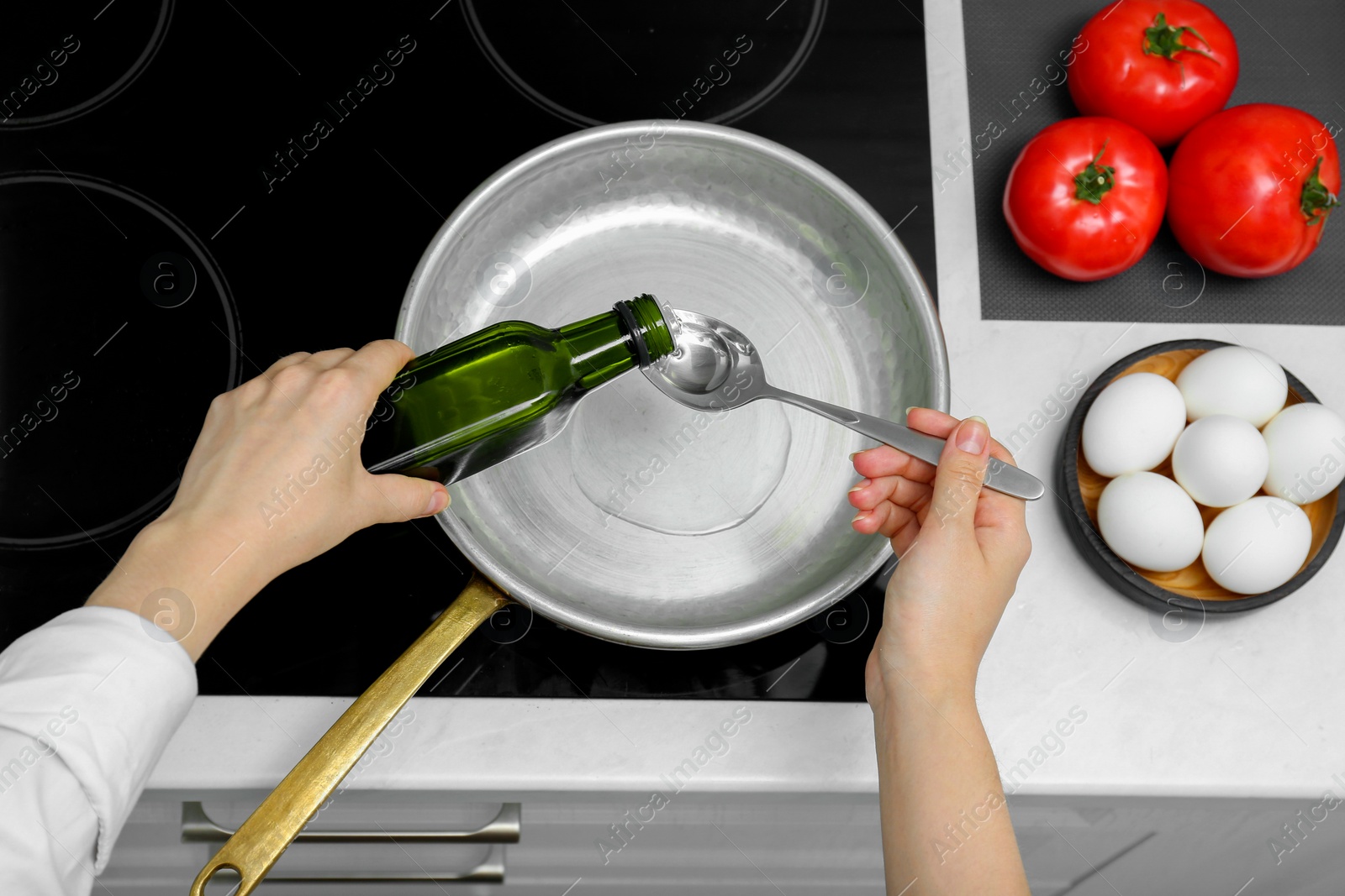 Photo of Woman pouring cooking oil from bottle into frying pan in kitchen, top view