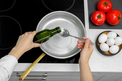 Photo of Woman pouring cooking oil from bottle into frying pan in kitchen, top view