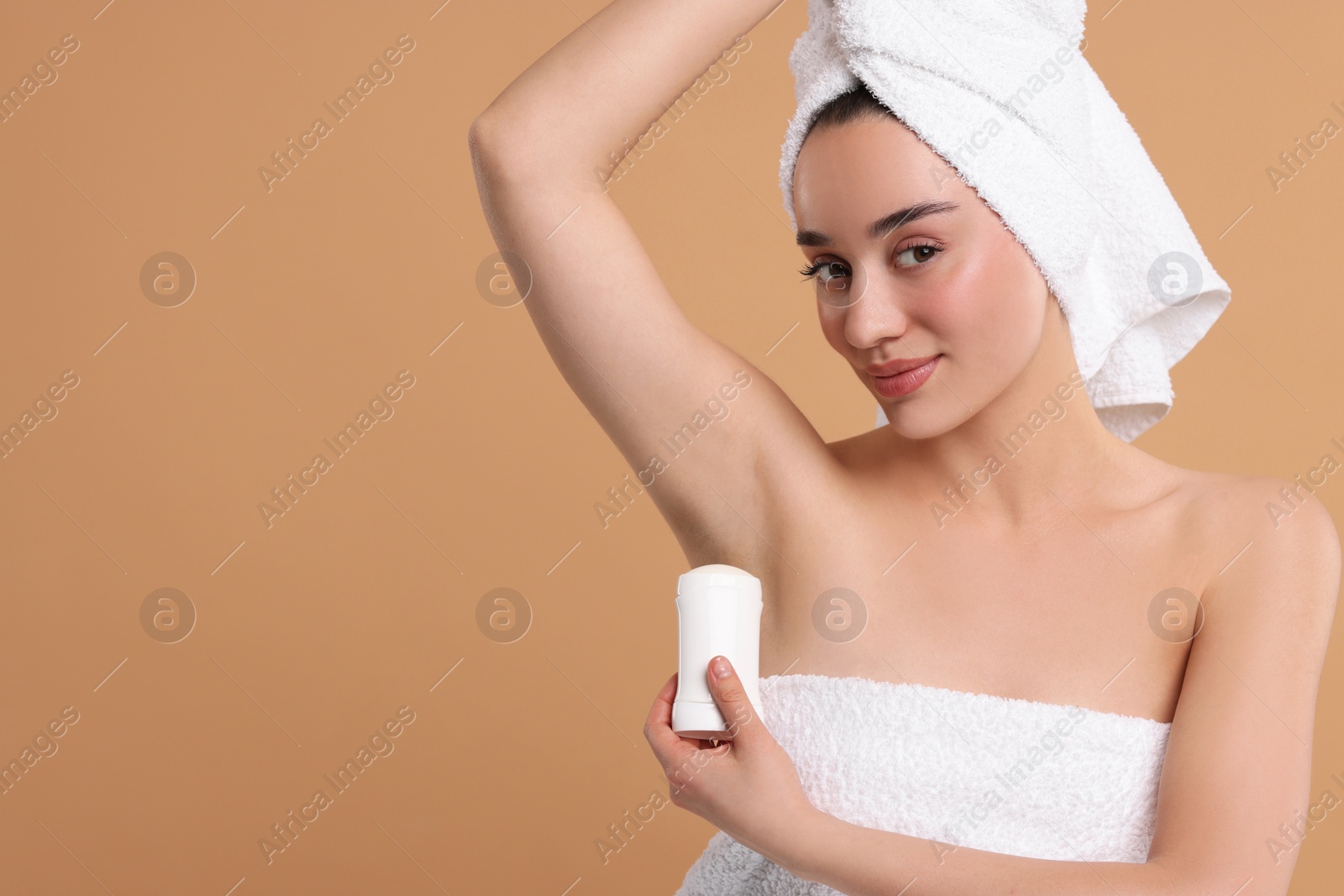 Photo of Beautiful woman applying deodorant on beige background, space for text