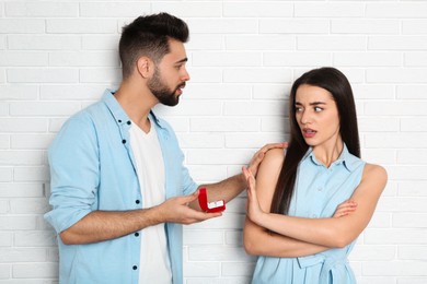 Young woman rejecting engagement ring from boyfriend near white brick wall
