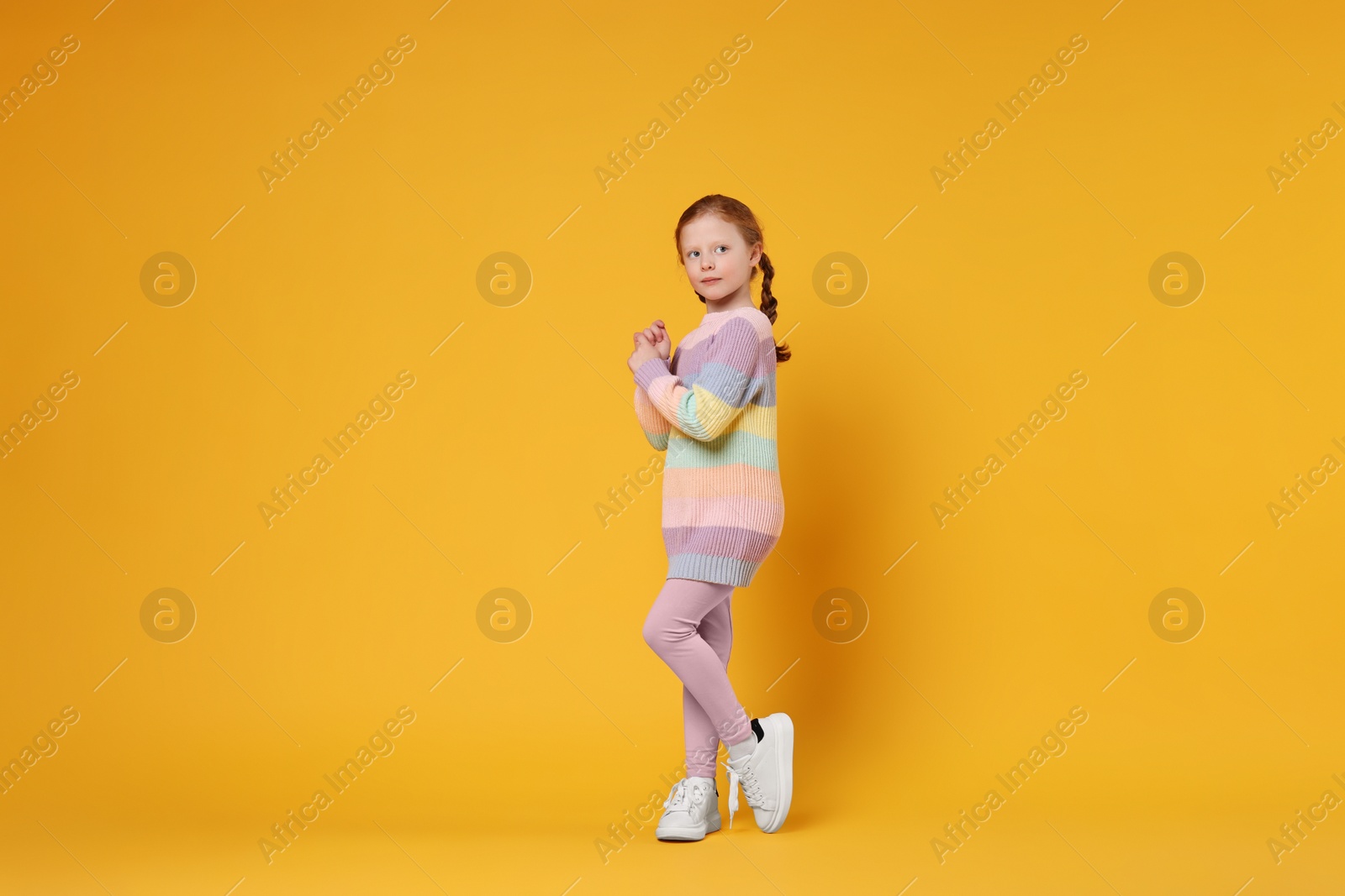 Photo of Cute little girl dancing on orange background