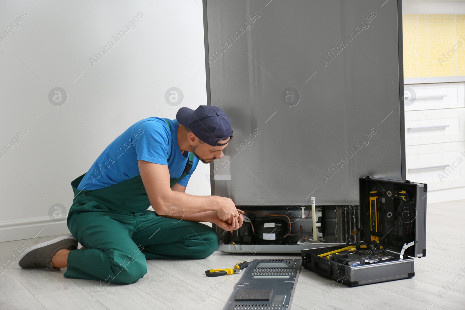 Photo of Male technician with pliers repairing refrigerator indoors