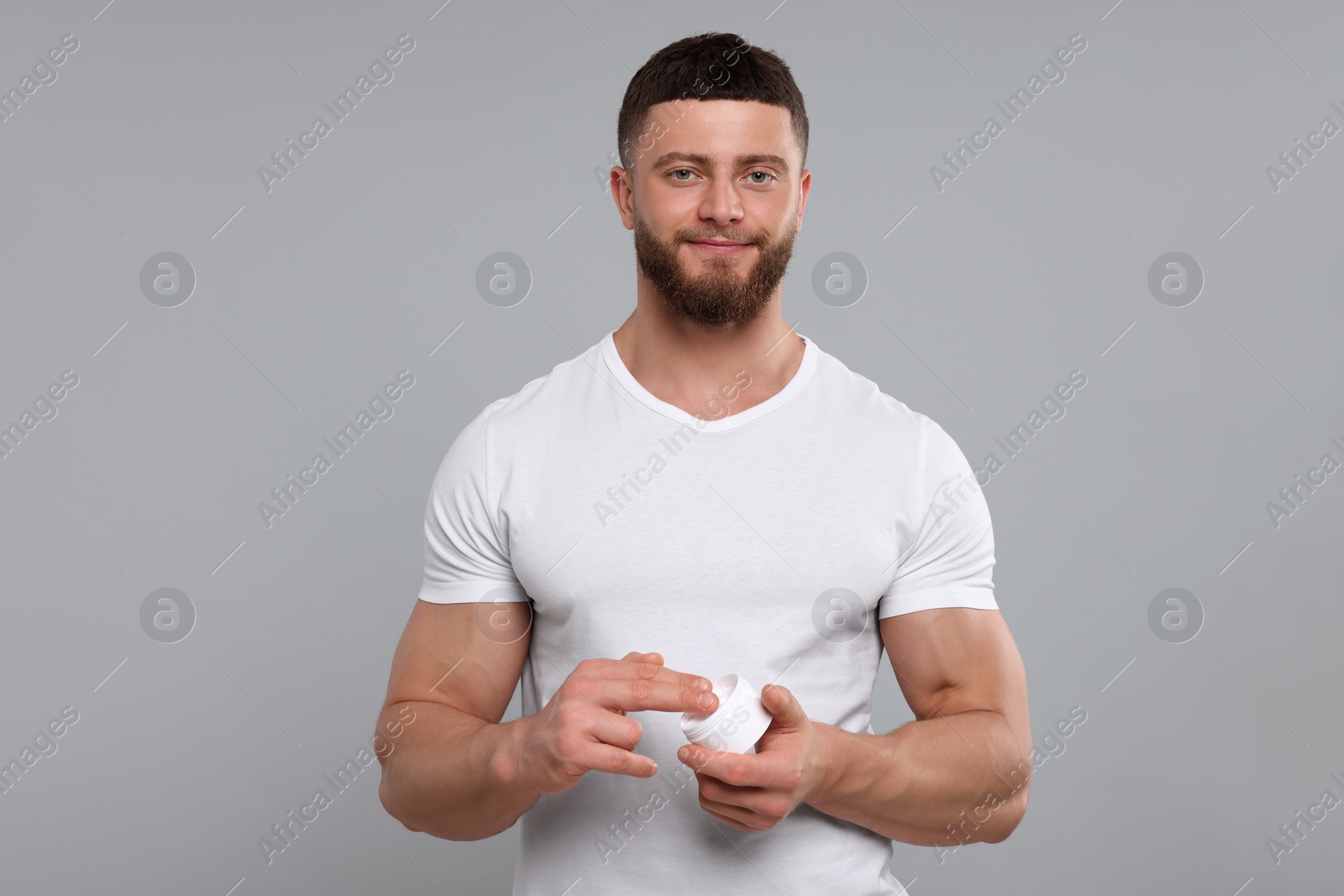 Photo of Handsome man applying body cream on light grey background