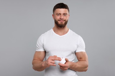 Handsome man applying body cream on light grey background