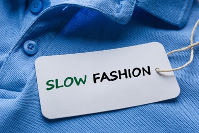 Image of Conscious consumption. Tag with words Slow Fashion on blue shirt, closeup