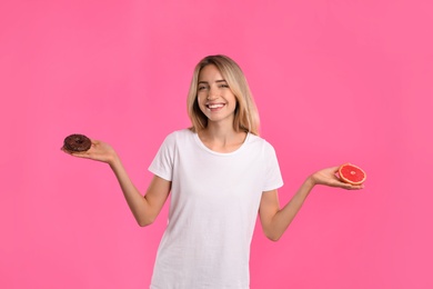 Photo of Woman choosing between doughnut and healthy grapefruit on pink background