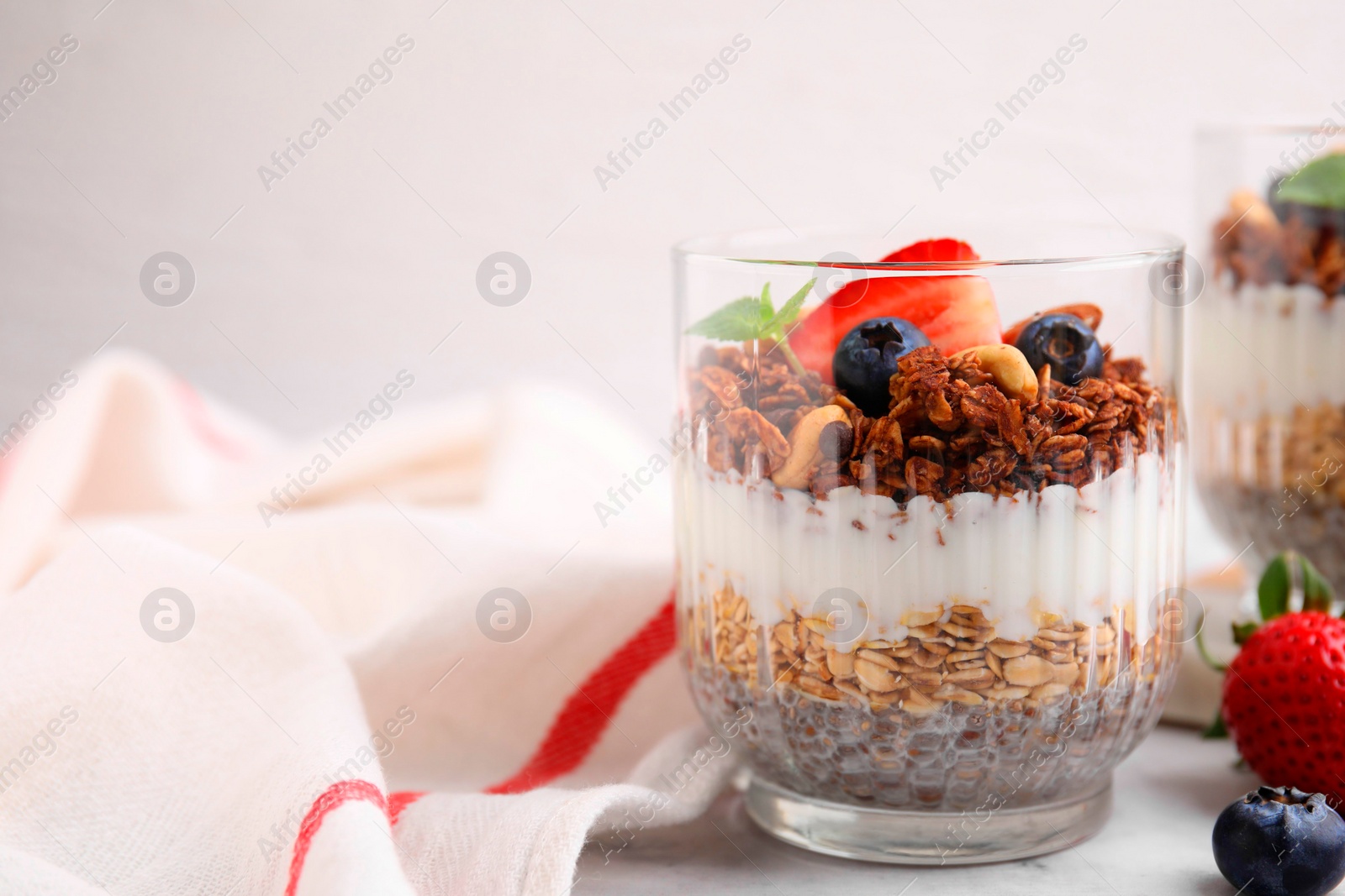 Photo of Tasty granola with berries, nuts, yogurt and chia seeds in glass on white table, space for text