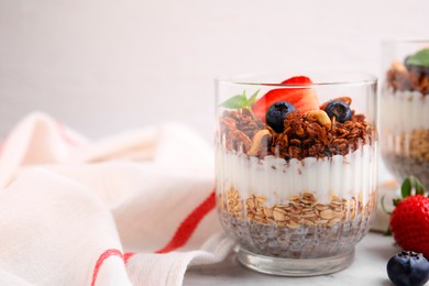 Photo of Tasty granola with berries, nuts, yogurt and chia seeds in glass on white table, space for text