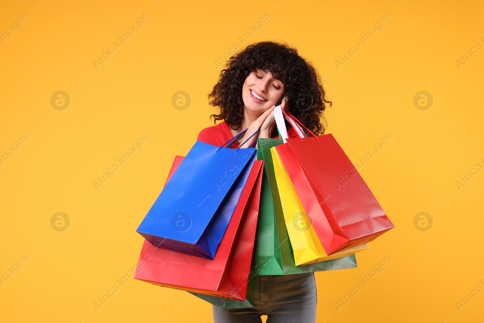 Photo of Happy young woman with shopping bags on yellow background