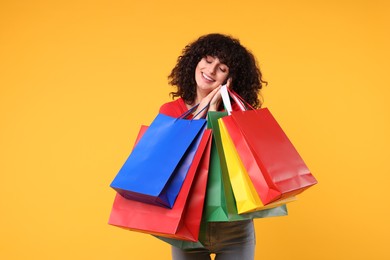 Happy young woman with shopping bags on yellow background