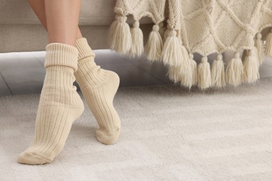 Woman wearing warm knitted socks at home, closeup. Space for text