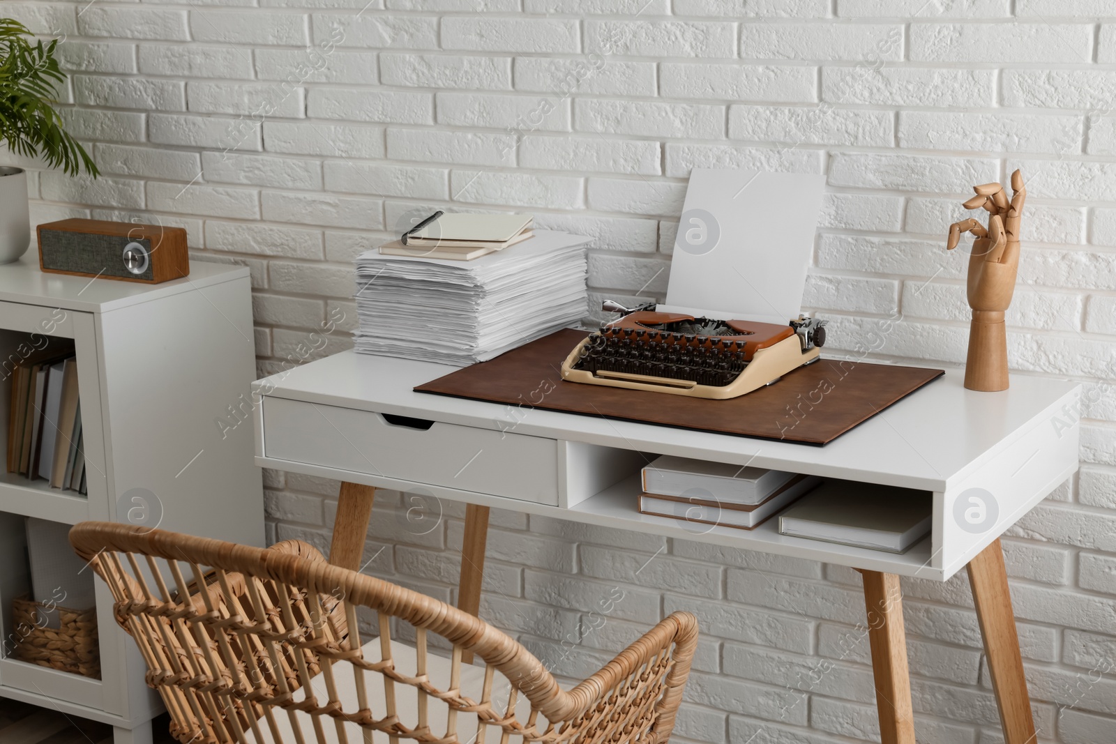 Photo of Comfortable writer's workplace with typewriter on desk near white brick wall