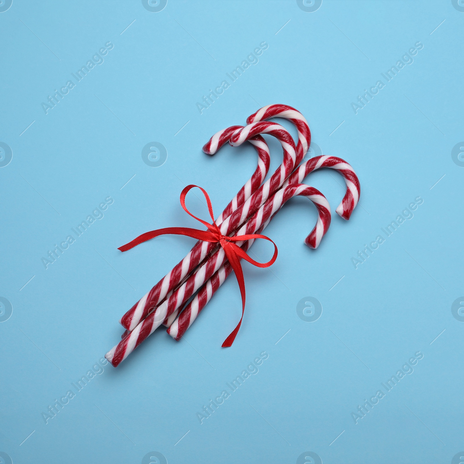 Photo of Sweet Christmas candy canes with red bow on light blue background, top view